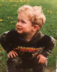 a young boy in a camouflage shirt crouching in the grass